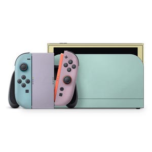 Puede incluir: Una consola de videojuegos en colores pastel con mandos desmontables. La consola presenta un cuerpo verde claro con una parte superior amarilla. Los mandos son de color azul claro y rosa, con botones negros. Diseñada para jugar de forma portátil o en base.
