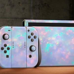 May include: A Nintendo Switch console and controller with a light blue and iridescent opal-like design. The console and controller are on a wooden surface.