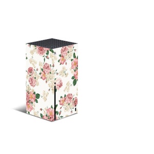 May include: A white gaming console with a floral design featuring pink and white flowers. The console has a black front panel with a small black button.