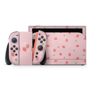 May include: A pink Nintendo Switch console and controllers with a strawberry pattern. The controllers are detached, showing the buttons and joysticks. The console and controllers are decorated with red strawberries and white flowers.
