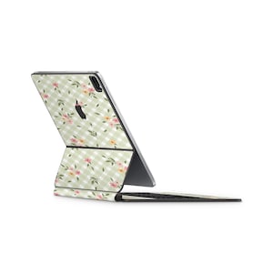 Pode incluir: Uma capa para iPad xadrez verde e branco com um padrão floral. A capa está dobrada ao meio e o iPad está fechado.