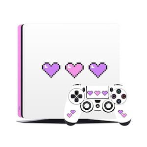 May include: A white PlayStation 4 console and controller with pink and purple pixelated heart designs. The console has a pink border and the controller has hearts on the front and back.