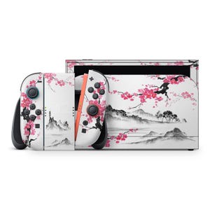 May include: A white Nintendo Switch console and controllers with a Japanese-inspired design. The design features pink cherry blossoms, mountains, and a black ink-style landscape. The controllers have black and coral accents.