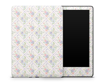 Può includere: Un e-reader con una cover a fantasia floreale. La cover presenta un motivo ripetuto di fiori pastello rosa, blu e viola, su uno sfondo color crema con una griglia lilla chiaro. Lo schermo dell'e-reader è nero.