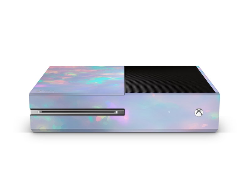 Puede incluir: Una consola Xbox One blanca con un dise&ntilde;o de &oacute;palo iridiscente. La consola tiene un panel frontal negro con un dise&ntilde;o texturizado.