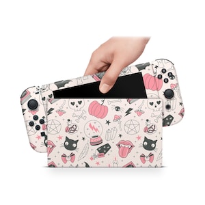 May include: A pink and black Nintendo Switch console skin with a spooky Halloween theme. The design features a variety of cute and whimsical illustrations, including skulls, pumpkins, cats, stars, and crystals.