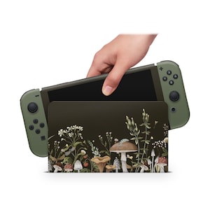 Op de afbeelding: Een groene Nintendo Switch-console met een aangepaste skin met een paddenstoel- en bloemenontwerp. De console is gesloten en wordt vastgehouden door een hand.