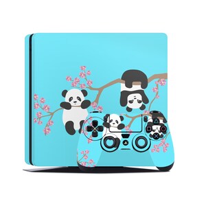 May include: A blue and white Playstation 4 console and controller skin with a panda bear design. The design features two pandas, one hanging upside down from a branch and the other sitting on the branch. The background is a light blue with pink cherry blossoms.