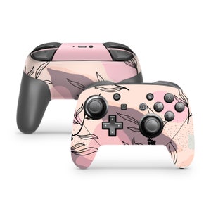 Op de afbeelding: Een roze en witte Nintendo Switch-controller met een bloemenpatroon. De controller heeft zwarte knoppen en joysticks.