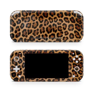Pode incluir: Uma capa para consola de jogos com estampa de leopardo. A capa apresenta um padrão de manchas marrons e pretas. A consola tem um ecrã preto e botões brancos. A parte superior e inferior da consola são visíveis.