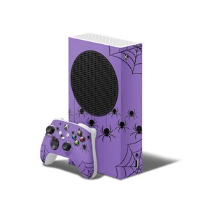 May include: A purple Xbox Series X console with a black spider web design and a matching purple controller. The console has a black speaker grille and a white Xbox logo.