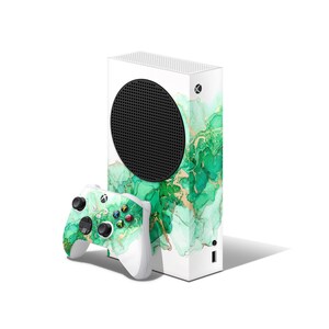 May include: White Xbox Series X console with a green and gold abstract design skin. The console is next to a white Xbox controller with a green and gold abstract design skin.