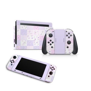 Pode incluir: Uma consola Nintendo Switch e comandos com um design de patchwork floral em tons de lavanda, rosa e branco. Os comandos têm detalhes em preto. O ecrã é preto.