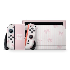 May include: A pink and white Nintendo Switch console featuring a bow design. The Joy-Con controllers are white with pink bows, and the main console has a pink and white striped pattern with bows. The buttons are black. The console is set against a white backdrop.