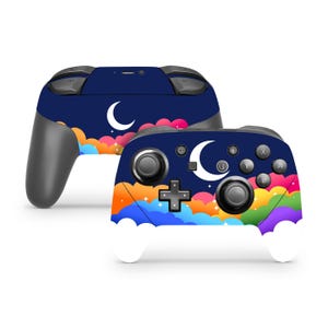 May include: Two video game controllers featuring a dark blue night sky design with a white crescent moon, small white stars, and colorful clouds in shades of pink, orange, yellow, green, and purple. The controllers have black buttons and joysticks.