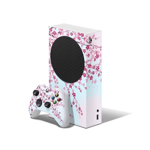 May include: A white Xbox Series X console with a pink and blue floral design. The console is shown with a matching white controller.