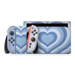 Op de afbeelding: Een Nintendo Switch-console en Joy-Con-controllers met een blauw-wit hartontwerp. De console en controllers hebben een lichtblauwe achtergrond met een hartvormig patroon in donkerder blauw. De Joy-Con-controllers zijn lichtblauw en wit.