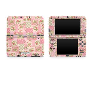 May include: A handheld gaming console featuring a pink and green patchwork pattern with strawberry and floral motifs. The device is shown from both the closed exterior view and the open interior view, displaying two black screens and control buttons.