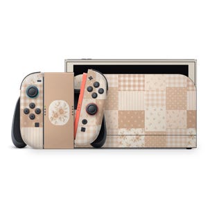 Puede incluir: Una consola de videojuegos y dos mandos con un patrón de patchwork en tonos beige y crema. El diseño incluye cuadrados con motivos de cuadros vichy, lunares y flores. La sección central del mando muestra una pequeña ilustración floral circular.