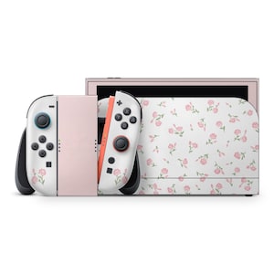 Puede incluir: Una consola Nintendo Switch con un diseño floral. La consola y los mandos son blancos con un patrón de flores rosas y hojas verdes. El cuerpo principal de la consola es rosa claro.