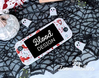 Op de afbeelding: Een witte Nintendo Switch Lite console met een aangepast ontwerp met rode bloedspatten en de tekst "Blood Design". De console ligt op een zwart-witte spinnenwebstof met witte spook stickers.