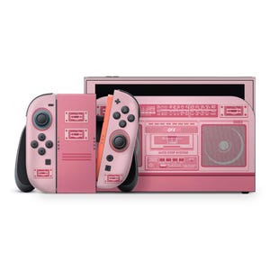 May include: A pink Nintendo Switch console with a retro boombox design. The Joy-Con controllers and the console itself feature a matching pink color scheme with a cassette tape and radio graphic. The design includes the text "OFX" and "AUTO STOP SYSTEM".