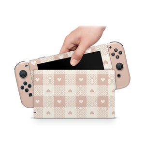 May include: A pink and white gingham Nintendo Switch console skin with a heart pattern. The skin is designed to fit the Nintendo Switch console and Joy-Cons.