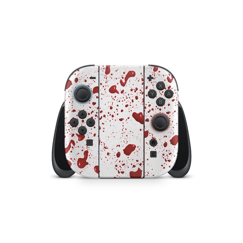 May include: A white Nintendo Switch controller with a pattern of red splatters. The controller has black joysticks and buttons, with a red button on the right side. The design covers the entire surface of the controller.