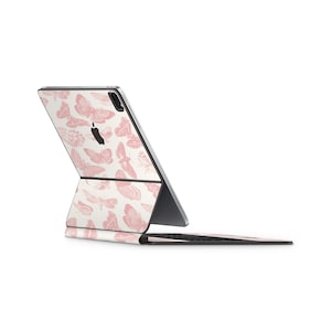 Pode incluir: Um iPad branco com um padrão de borboletas rosa nas costas e uma capa de teclado combinando. O iPad está fechado e o teclado está dobrado para trás.