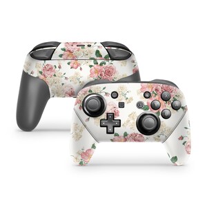 May include: A white Nintendo Switch controller with a floral design featuring pink and white flowers. The controller has black buttons and joysticks.