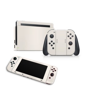 以下が含まれることがあります： 白いニンテンドースイッチ本体と白いJoy-Conコントローラー。本体は携帯モードで、Joy-Conは本体の右側に取り付けられています。