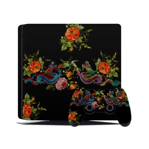 May include: Black gaming console and controller skin featuring an embroidered floral design with dragons, roses, and other flowers. The design includes red, orange, pink, green, and blue colors. The console and controller are set against a white background.