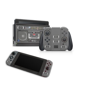 Pode incluir: Um console Nintendo Switch cinza e preto com uma pele personalizada que se assemelha a um boombox vintage. A pele apresenta um leitor de cassetes, um dial de rádio e botões. O console é mostrado com ambos os controladores Joy-Con esquerdo e direito conectados.