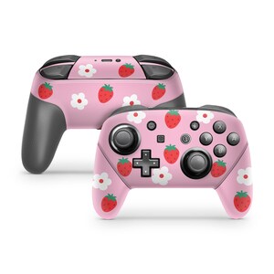 May include: A pink Nintendo Switch controller with a strawberry and flower pattern. The controller has a black faceplate and black buttons.