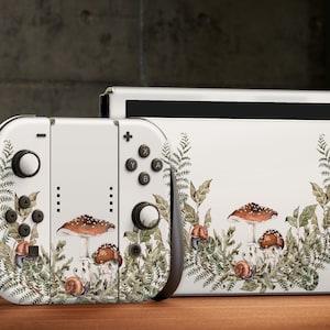 May include: White Nintendo Switch console and controller with a mushroom and fern design. The design features brown mushrooms with white spots, green ferns, and brown snails.