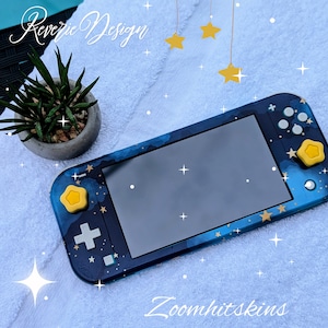 May include: A blue and gold Nintendo Switch Lite console with a starry night design. The console has a yellow star on the left joy-con and a yellow star on the right joy-con. The text "Reverie Design" is visible in the top left corner of the image. The text "Zoomhitskins" is visible in the bottom right corner of the image.