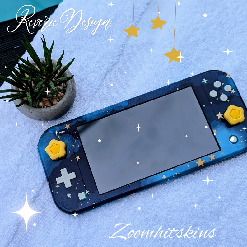 May include: A blue and gold Nintendo Switch Lite console with a starry night design. The console has a yellow star on the left joy-con and a yellow star on the right joy-con. The text "Reverie Design" is visible in the top left corner of the image. The text "Zoomhitskins" is visible in the bottom right corner of the image.