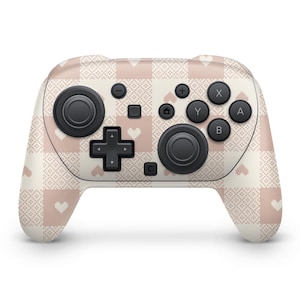 Könnte beinhalten: Ein kabelloser Videospiel-Controller mit einem cremefarbenen und rosa Herz- und geometrischen Muster. Der Controller hat schwarze Knöpfe und Joysticks. Das Design bedeckt den gesamten Controller.