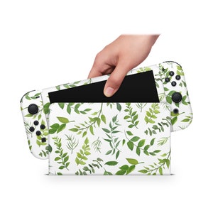 Op de afbeelding: Een witte Nintendo Switch-console met een groen bladerenpatroon op de achterkant. De console is gesloten en wordt vastgehouden door een hand.