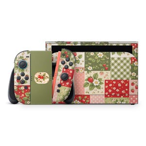 May include: A Nintendo Switch console and controllers with a patchwork strawberry design. The design features red, green, and pink squares with floral and strawberry patterns. The controllers have black buttons and joysticks.