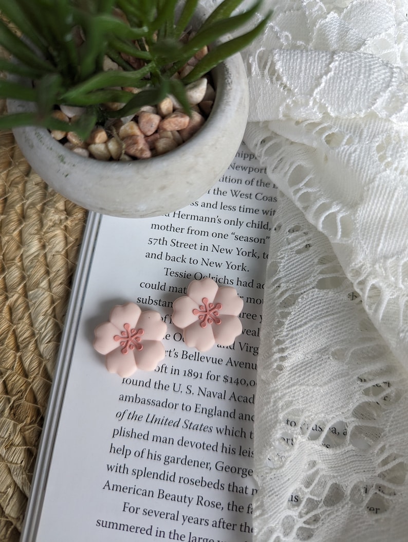 May include: Two pink flower-shaped hair clips with a light pink center. The clips are on a book with text about a historical figure.