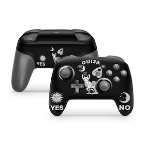 May include: A black and white Nintendo Switch controller with a Ouija board design. The controller features a black cat with a Ouija board planchette, a sun, a moon, and the words "YES" and "NO".