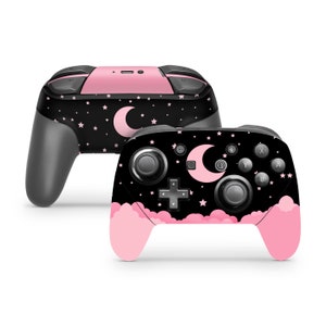 Op de afbeelding: Een zwarte en roze Nintendo Switch-controller met een maan- en sterrenontwerp. De controller heeft een roze wolkontwerp aan de onderkant.