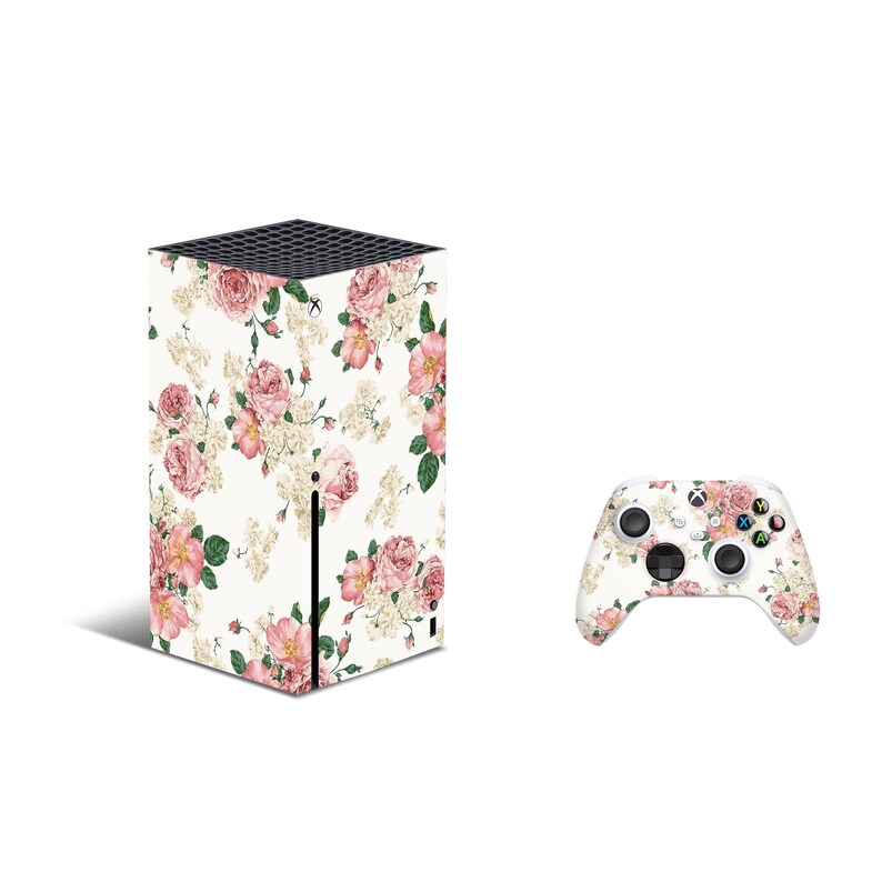May include: A white gaming console with a floral design featuring pink roses and green leaves. The console is next to a matching white gaming controller with the same floral design.