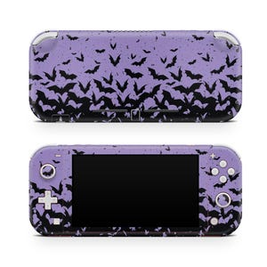 May include: A purple handheld gaming console with a black bat pattern. The console has a black screen, buttons, and control sticks. The bat design covers the entire console, creating a spooky aesthetic.