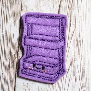 May include: Purple felt shelf with a cute face embroidered on the bottom. The shelf has three levels.