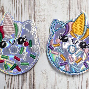May include: Two embroidered unicorn patches with iridescent fabric. Each patch features a smiling unicorn face with a colorful horn, eyelashes, and sprinkles. The patches are outlined with a decorative stitch.
