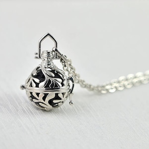 Può includere: Collana d'argento con un delicato ciondolo ornato a forma di gabbia con un motivo a foglie. Il ciondolo è attaccato a una catena d'argento.