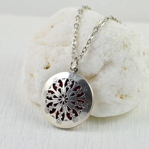 May include: Silver necklace with a round pendant featuring a delicate, intricate design. The pendant has a filigree pattern with a red centre.