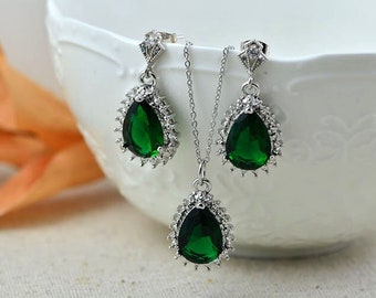 May include: A silver necklace and earrings set with teardrop-shaped green gemstones surrounded by smaller clear stones.